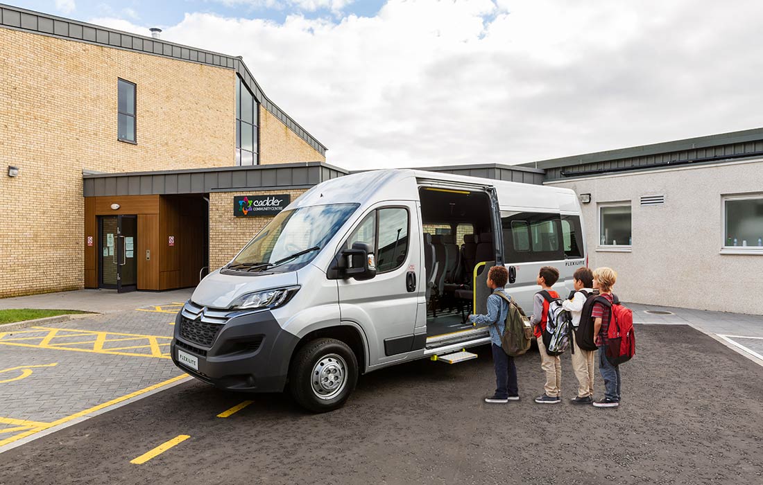 A FlexiLite minibus parked in front of a school with children boarding